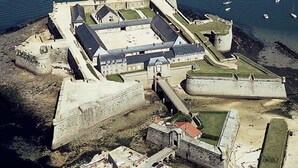 An aerial view of a fortified structure with multiple buildings, a large courtyard, and a surrounding moat.