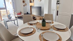 Un coin repas avec une table ronde dressée pour quatre personnes, entourée de sets de table en fibres tressées, et une télévision en arrière-plan.