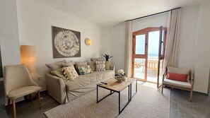Sala de estar con sofá, sillón, mesa de centro y vista al exterior a través de puertas correderas de vidrio.