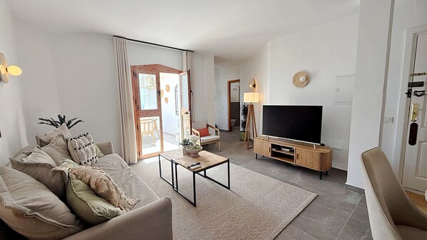 Una sala de estar moderna con sofá, mesa de centro, televisor y comedor.