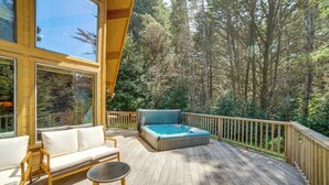 A wooden deck with a hot tub, a sofa, and a table. - Hot Tub, 1 Mi to Beach: 12-Acre Fort Bragg Cabin! (Fort Bragg)