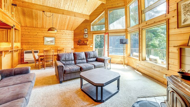 A spacious wooden cabin with a large living area featuring a sofa, a coffee table, and a dining table with chairs. - Hot Tub, 1 Mi to Beach: 12-Acre Fort Bragg Cabin! (Fort Bragg)