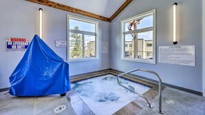 A spa room with a hot tub, wooden beams, large windows, and safety signs. - Sugar Ski in/out 1BR 1BA views/pool/sauna/hot tub (Sugar Mountain)