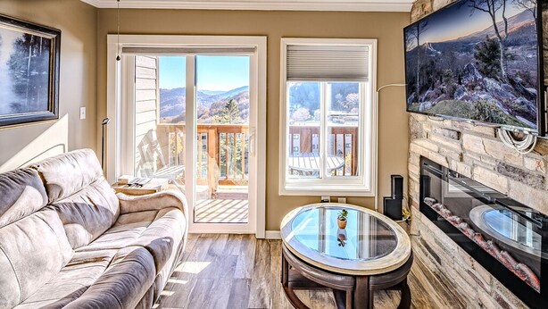 A living room with a leather sofa, a glass coffee table, a fireplace, and a TV mounted on the wall. - Sugar Ski in/out 1BR 1BA views/pool/sauna/hot tub (Sugar Mountain)