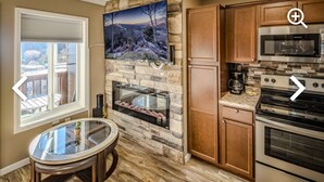 A kitchen with a stone backsplash, a flat-screen TV, wooden cabinets, a built-in oven, and a glass table. - Sugar Ski in/out 1BR 1BA views/pool/sauna/hot tub (Sugar Mountain)