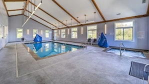 An indoor swimming pool with a concrete floor, wooden beams, and large windows. - Sugar Ski in/out 1BR 1BA views/pool/sauna/hot tub (Sugar Mountain)