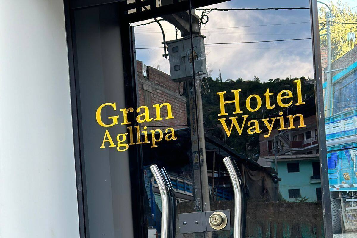 A hotel entrance with glass doors and a metal handle. The name 'Gran Agllipa Hotel Wayin' is visible on the glass.