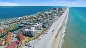 An aerial view of a coastal resort with beachfront properties, a marina, and a long sandy beach.