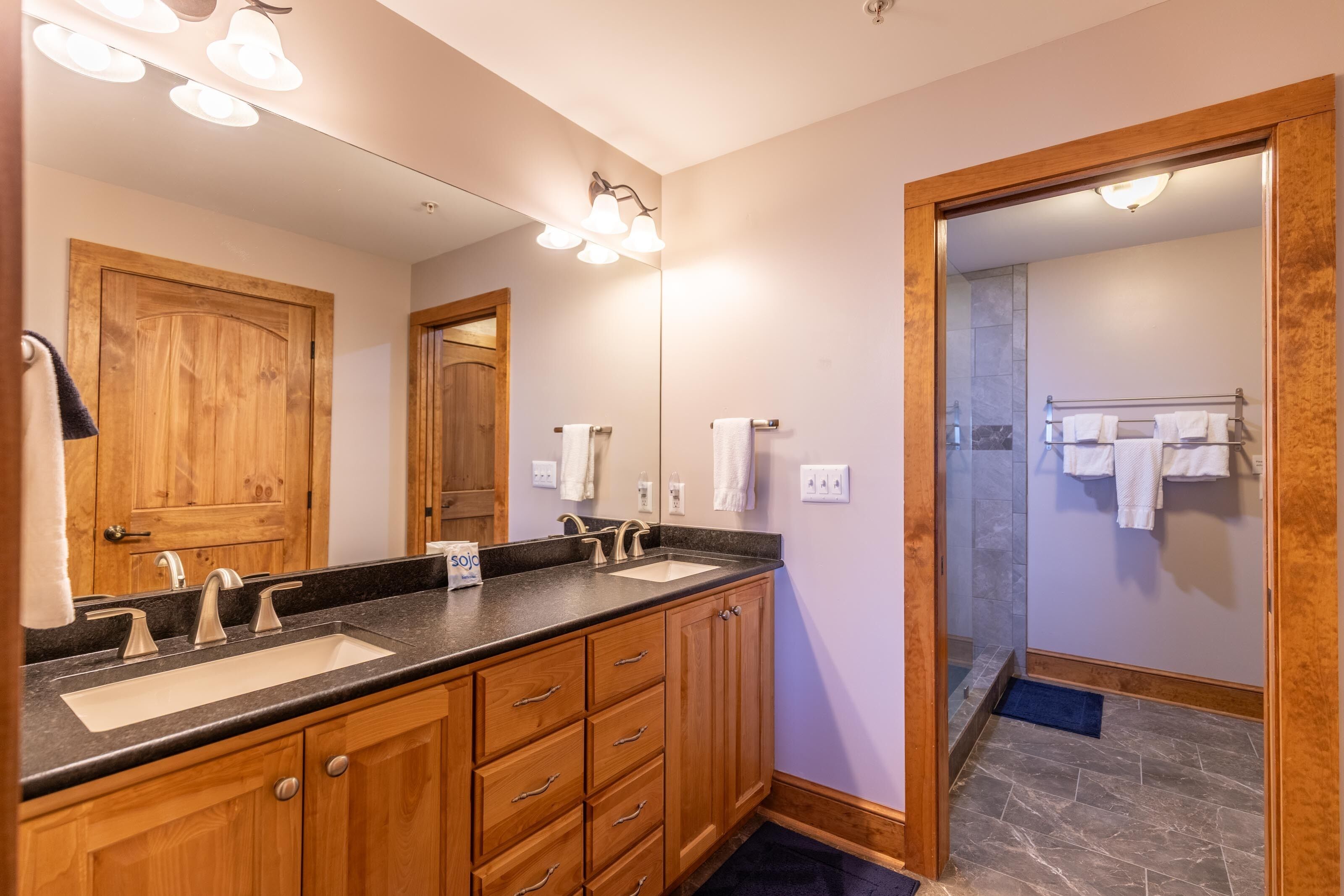Une salle de bain avec un double vasque, des meubles en bois, un grand miroir et un espace douche.