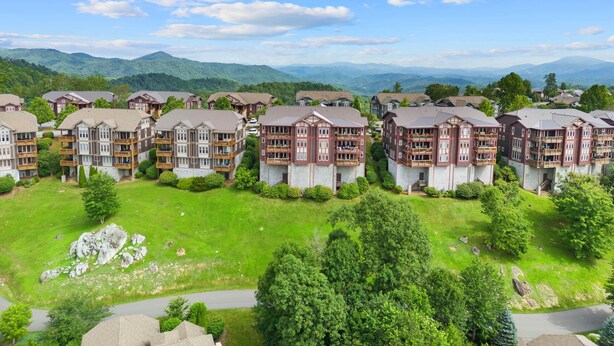 A cluster of multi-story buildings with balconies, set against a backdrop of green hills and a clear blue sky. - Mayway Retreat - Echota Club Amenities, Beautiful Mountain Views (Banner Elk)