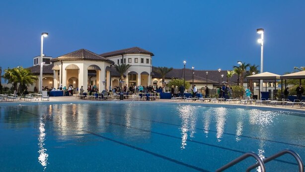 A swimming pool with lounge chairs and umbrellas, a building with arches, and palm trees. - 6BR resort home with private pool, game room & golf access. (Kissimmee)