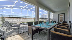 A covered patio with outdoor furniture, a pool, and a view of the surrounding landscape. - 6BR resort home with private pool, game room & golf access. (Kissimmee)