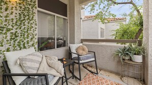 A balcony with a sofa, a chair, and a small table. There is a window with blinds, a wall covered in ivy, and a potted plant on a metal stand. -  Best Scottsdale location. Shopping, Food, Golf, near (Scottsdale)