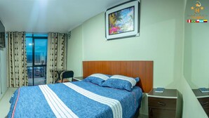 A hotel room with a bed, a nightstand, a chair, a TV, and a window with curtains. - HOTEL TERRA (Ayacucho)