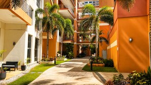 Un edificio de varios niveles con zonas de estar al aire libre, palmeras y un paseo central.