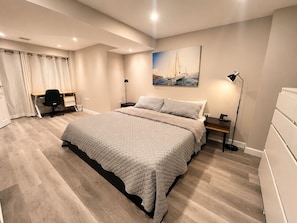 A modern bedroom with a large bed, a desk, a chair, and a painting on the wall.