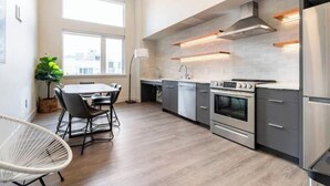Eine moderne Küche mit Edelstahlgeräten, ein Essbereich mit rundem Tisch und Stühlen sowie große Fenster, die für natürliches Licht sorgen.