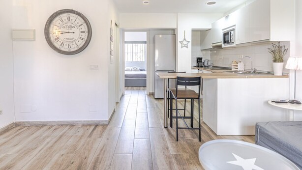 A modern kitchen with a central island, a dining area with two chairs, and a large wall clock. - RentitSpain · Little Paradise on the Costa del Sol (Torremolinos)