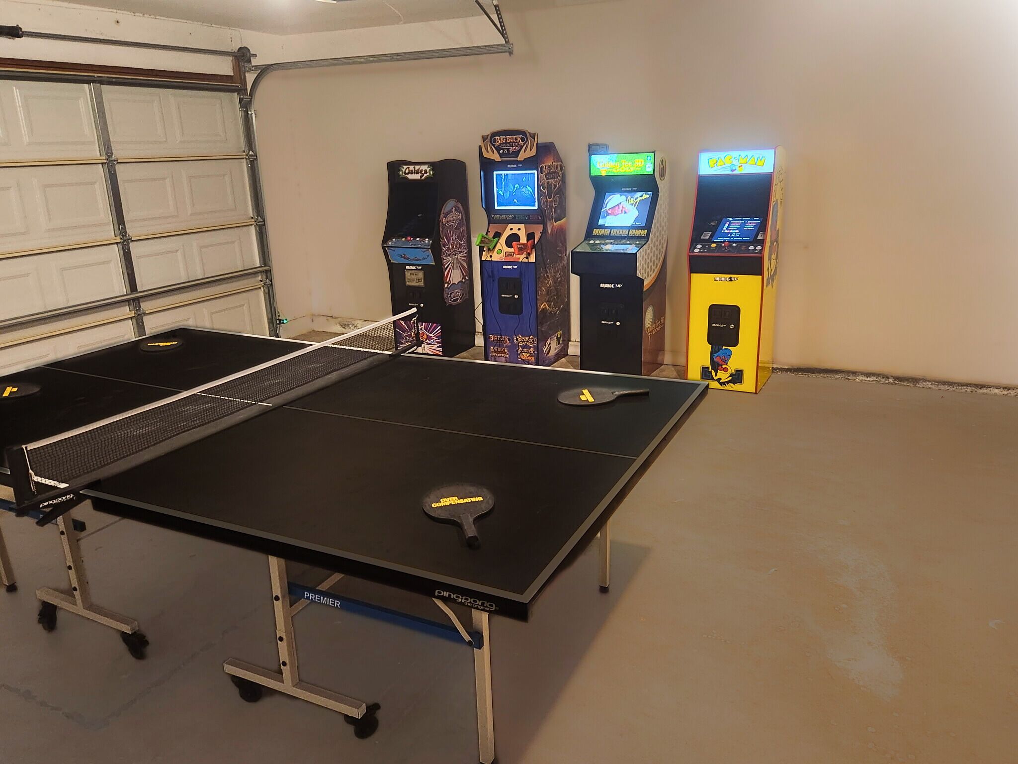 Ett bordtennisbord i ett garage, med arkadspel synliga i bakgrunden.