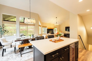 A modern kitchen with a large island, dining area with chairs, and a view of the outdoors.
