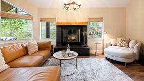 Ein Wohnzimmer mit Kamin, Ledersofas, einem runden Couchtisch und großen Fenstern.