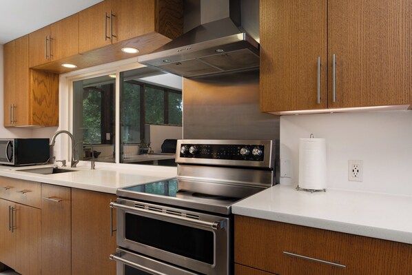 A modern kitchen with stainless steel appliances, wooden cabinets, and a large window providing natural light.
