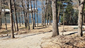 Un terrain de camping ombragé, avec un sol sablonneux et un lac en arrière-plan.