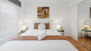 Une chambre d’hôtel avec un grand lit, deux tables de chevet avec des lampes, un grand miroir et un tableau au mur.