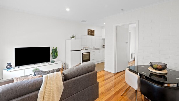 Un salon moderne avec un téléviseur à écran plat, un canapé gris et un coin repas comprenant une table et des chaises noires.