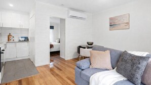Un espace de vie compact comprenant un coin cuisine, un coin repas et un espace détente avec un canapé et un tableau au mur.