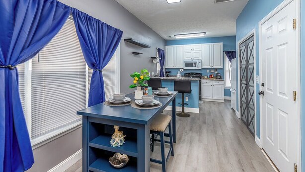 A modern kitchen with white cabinets, a blue dining table, and blue curtains. - Five-Minutes Flyover Cherry Point NC (Havelock)