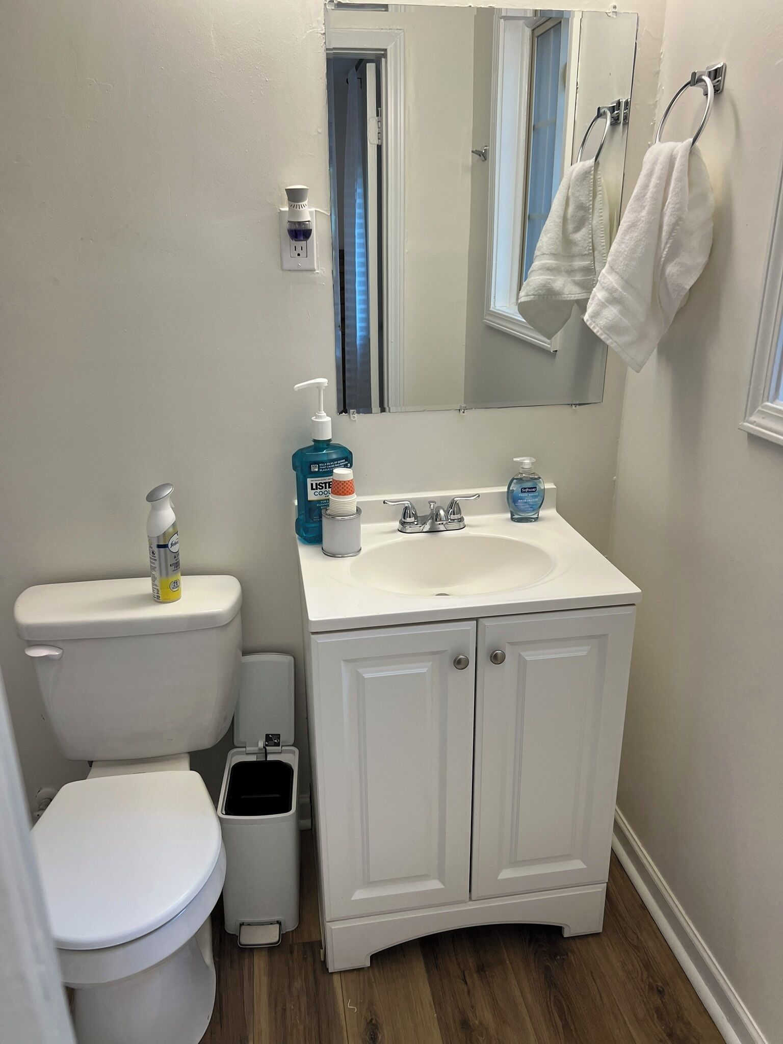 A bathroom with a white toilet, a sink with a mirror above it, and a trash bin.