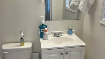 A bathroom with a white toilet, a sink with a mirror above it, and a trash bin.