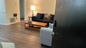 Un salon avec un canapé marron, un fauteuil gris, une table basse en bois et une lampe.