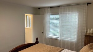 Une chambre à coucher avec un lit, une fenêtre avec des stores, une porte et une petite fenêtre au-dessus de la porte.