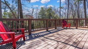 Une terrasse en bois, agrémentée de deux fauteuils Adirondack rouges, entourée d’une balustrade en bois, et offrant une vue sur une zone boisée.