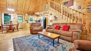 A spacious wooden cabin with a dining area, two leather sofas, a coffee table, and a staircase leading to an upper level. - Stunning Surroundings, Hot Tub Soaks, S'mores & Nearby Attractions - Our Favorite Place (Blue Ridge)