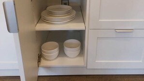 Une cuisine avec des meubles blancs, une étagère où sont empilées des assiettes et deux bols sur une étagère inférieure.