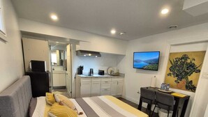 Une chambre à coucher de taille réduite comprenant un lit, un bureau, une chaise, un téléviseur et un coin cuisine.
