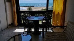 Une pièce avec un canapé, une table en verre et une vue sur la plage, visible à travers une grande fenêtre.