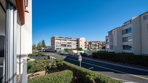 A multi-story residential building with balconies, a clear sky, and a road in the foreground. - Apartment located 100 m from the beach, with a pool and parking (Agde)