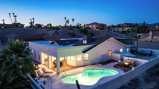 Una casa moderna con piscina, muebles de patio y un coche aparcado cerca.