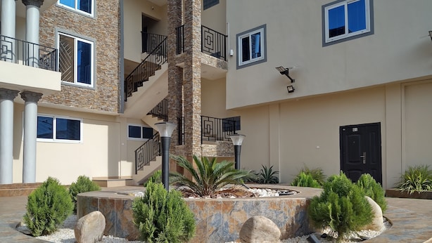 Un edificio de varios pisos con un patio central que presenta una plataforma circular de piedra, palmeras y una escalera.