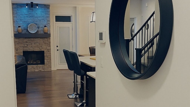 A hallway with a wooden floor leading to a dining area with a table and chairs. A round mirror is mounted on the wall. - Welcome to our Luxury Nest…A home away from home. Your comfort is our culture (Airdrie)