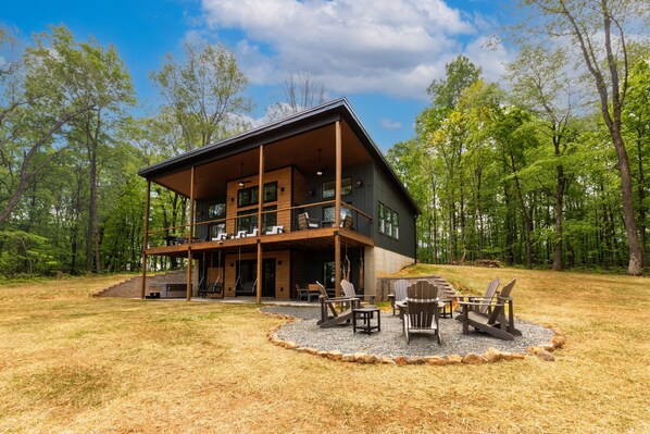 Eine moderne, zweistöckige Holzhütte mit überdachter Veranda und Sitzbereich im Freien.