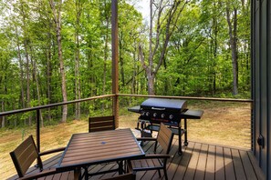 Eine Terrass mit Grill und Sitzgelegenheit mit Blick auf einen Wald.