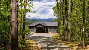 Un chalet avec une allée de gravier menant à un bâtiment de couleur sombre, entouré de grands arbres.