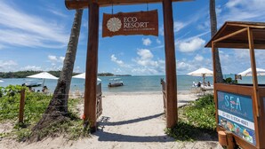 A wooden archway with a sign reading "ECO RESORT Praia dos Carneiros" leading to a beach with umbrellas and a boat in the background. - Mare Nostrum - Carneiros Beach - Ocean View - Balcony - 2 Suites - Eco Resort Condominium (Tamandare)