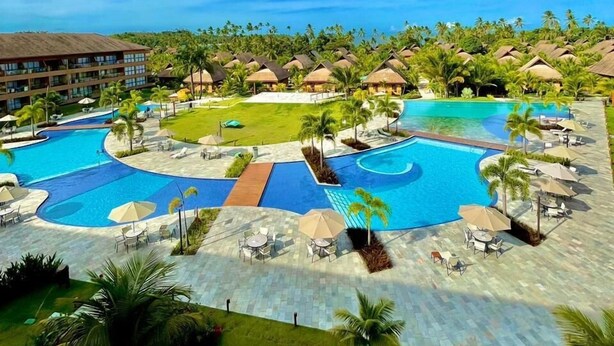 A resort with multiple swimming pools, palm trees, and thatched-roof huts. - Mare Nostrum - Carneiros Beach - Ocean View - Balcony - 2 Suites - Eco Resort Condominium (Tamandare)