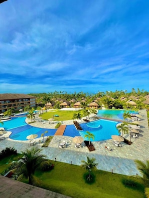 Ein Resort mit mehreren Schwimmbecken, Palmen und Hütten mit Reetdächern.